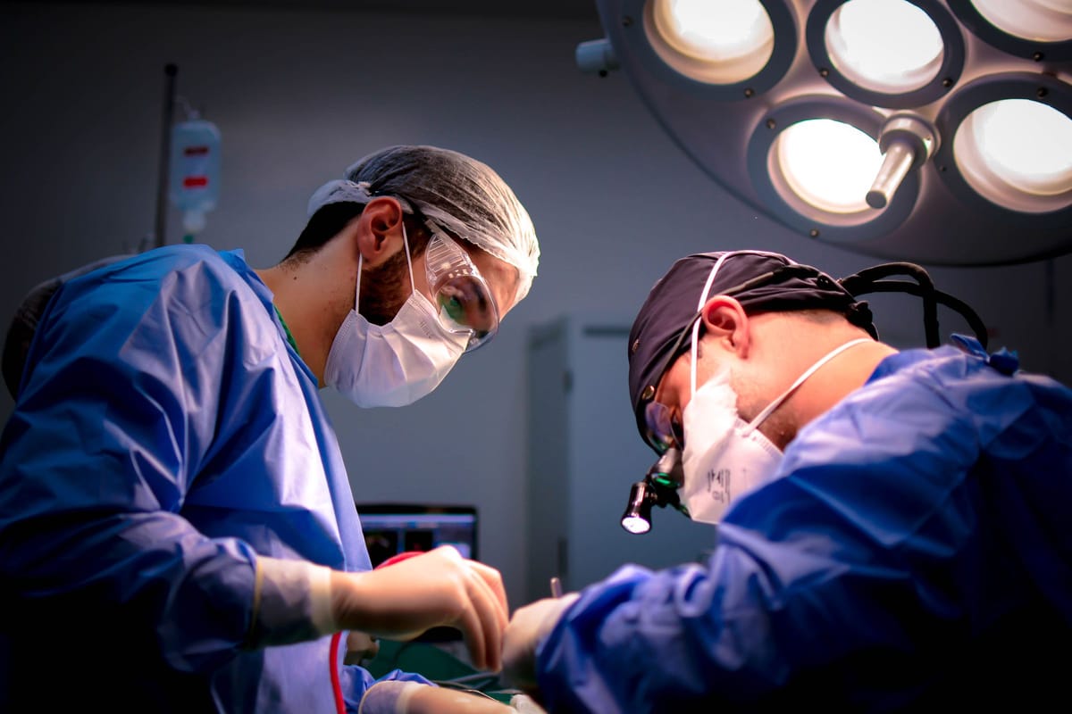 Two surgeons in blue scrubs operating under theatre lights