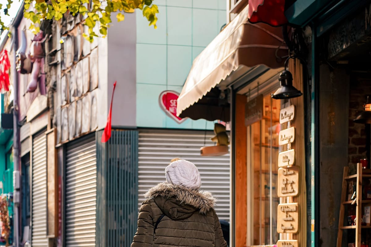 A shopper walking past closed roller shutters on a narrow shopping street